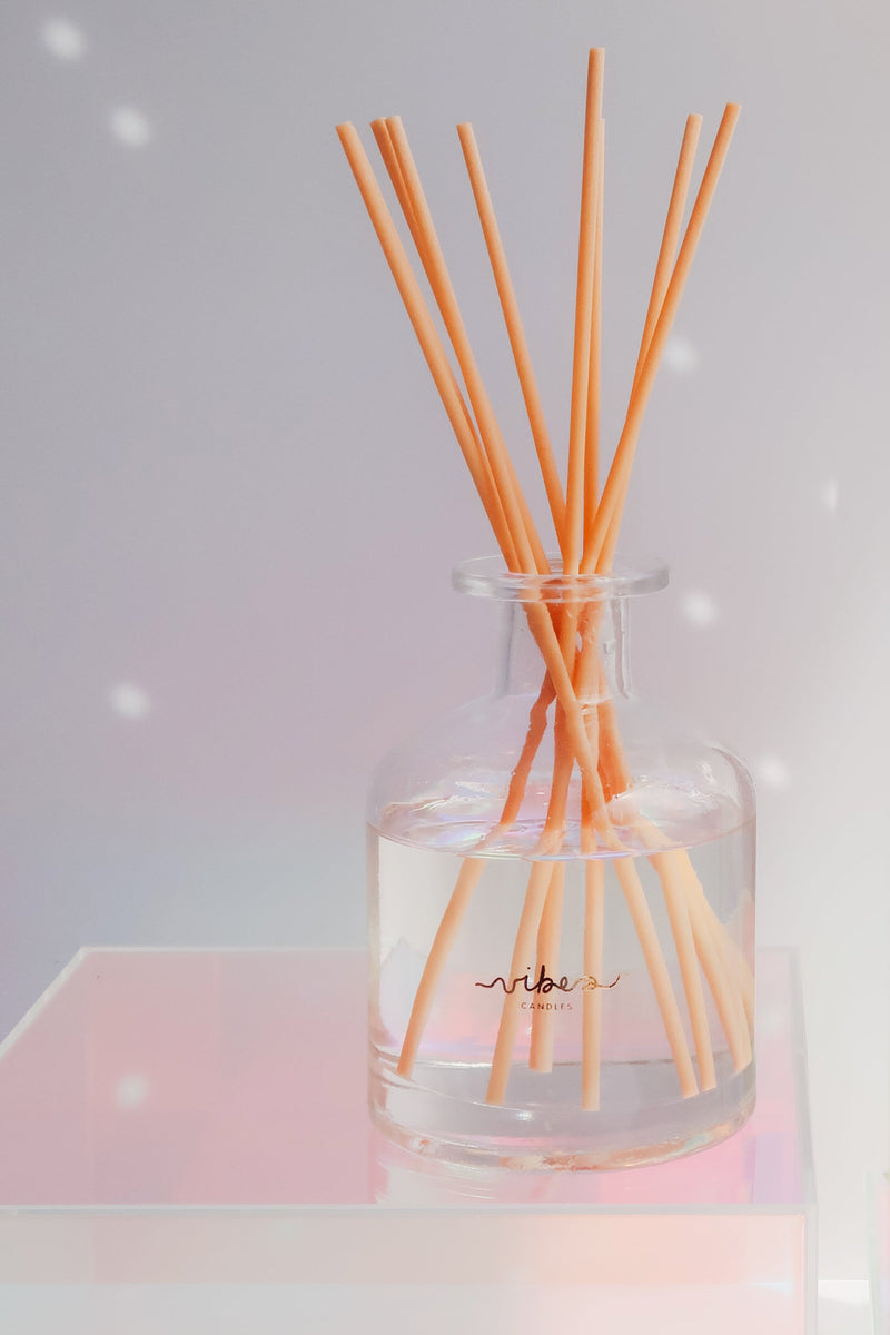 Clear glass diffuser with Reed sticks on a light pink surface and light gray background
