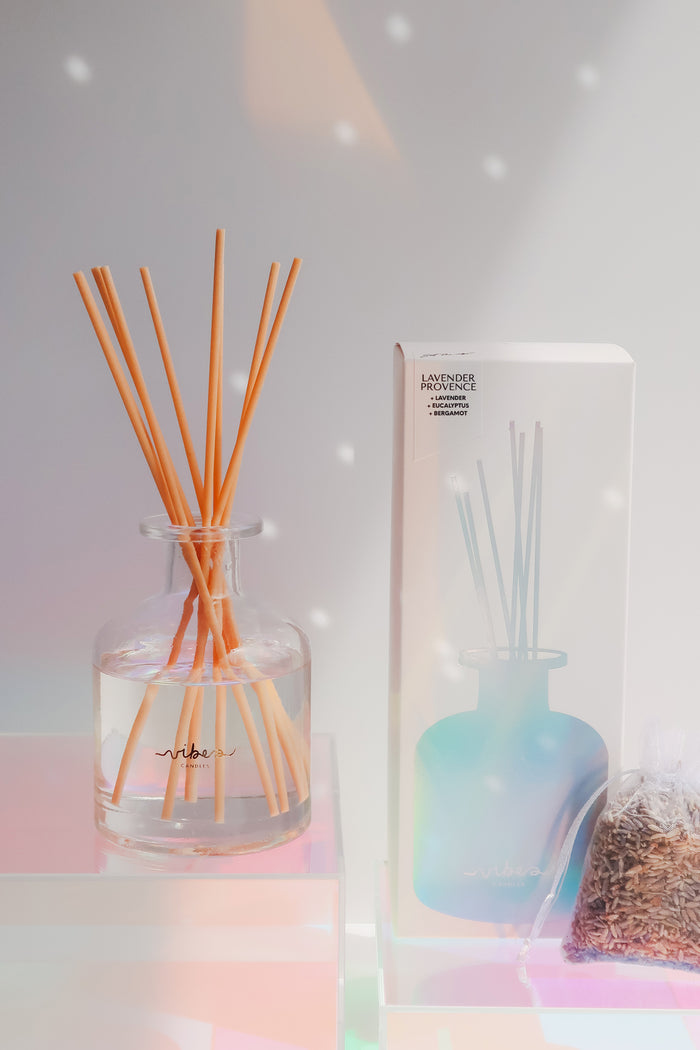 Reed diffuser set with clear glass bottle and wooden sticks, next to its packaging on a soft background.